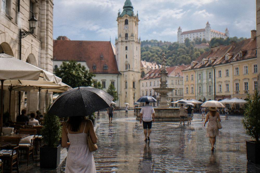 People with umbrellas walking a Bratislava street during a summer rain shower