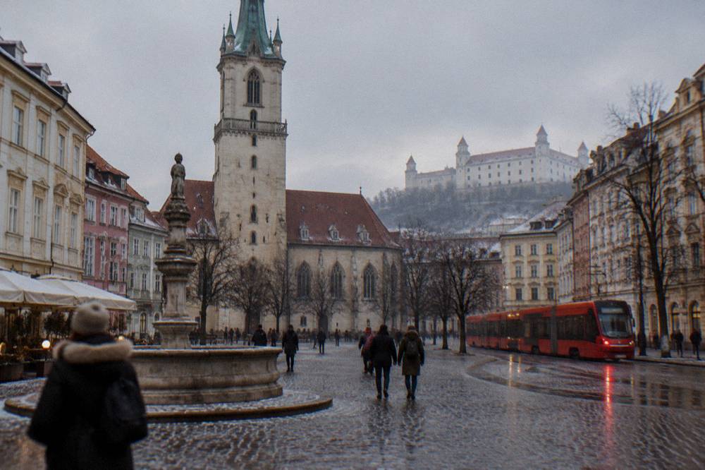 A red tram passing buildings on a wet Bratislava street