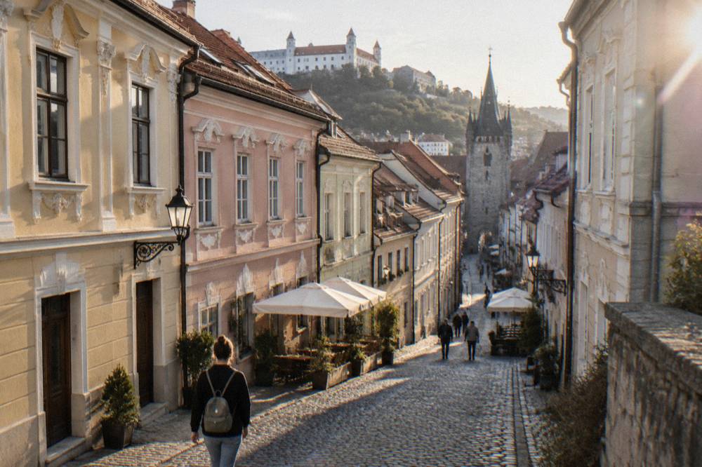 Cobblestone street in Bratislava Old Town with a visitor carrying a small backpack past colourful baroque facades