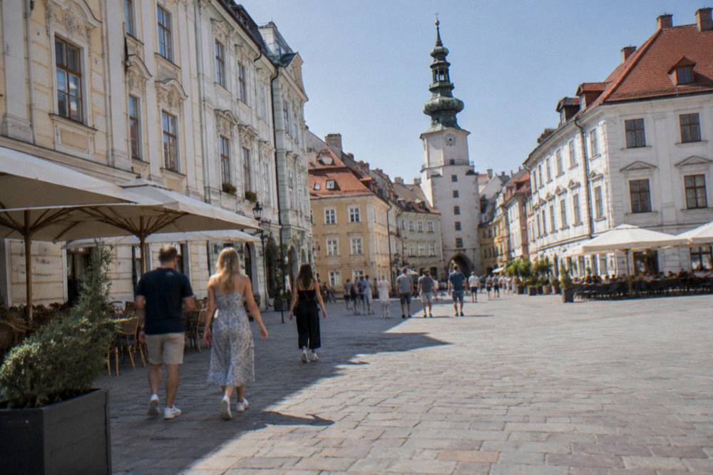 Visitors without bags walking across the main square of Bratislava Old Town on a sunny afternoon