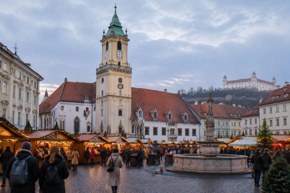 Festive wooden huts with warm lighting crowded together on a city square in evening