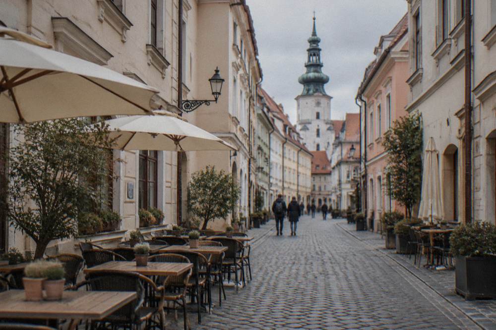 A narrow Old Town street in Bratislava lined with small shops and café tables