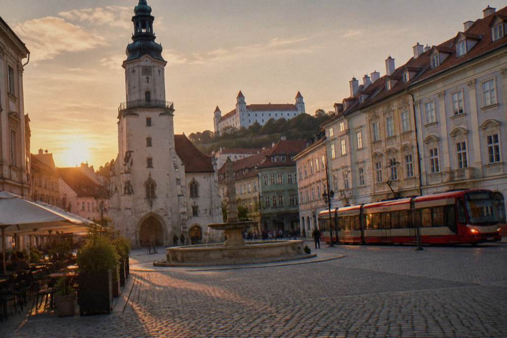 A tram passing lit buildings on a Bratislava street in the evening