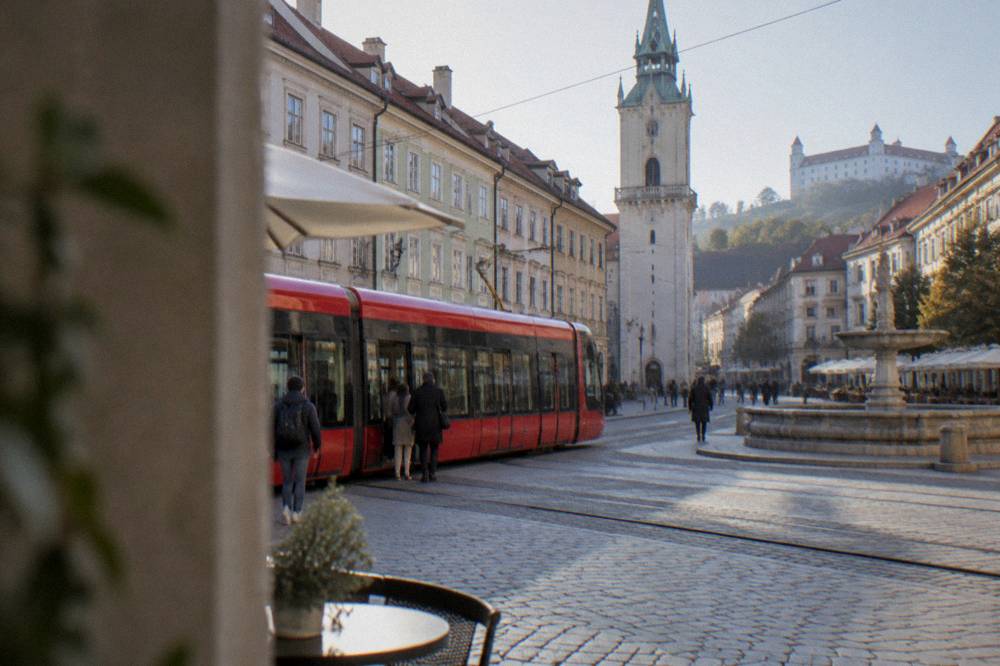 A red tram moving along a street in Bratislava with passengers boarding