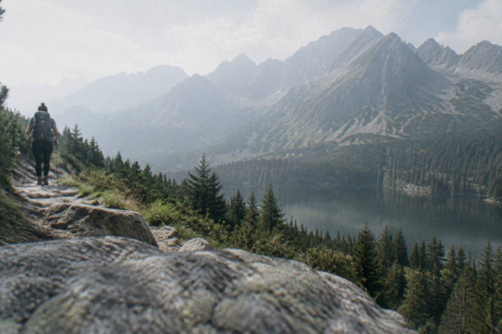 A hiker on a mountain trail above forested slopes in the High Tatras