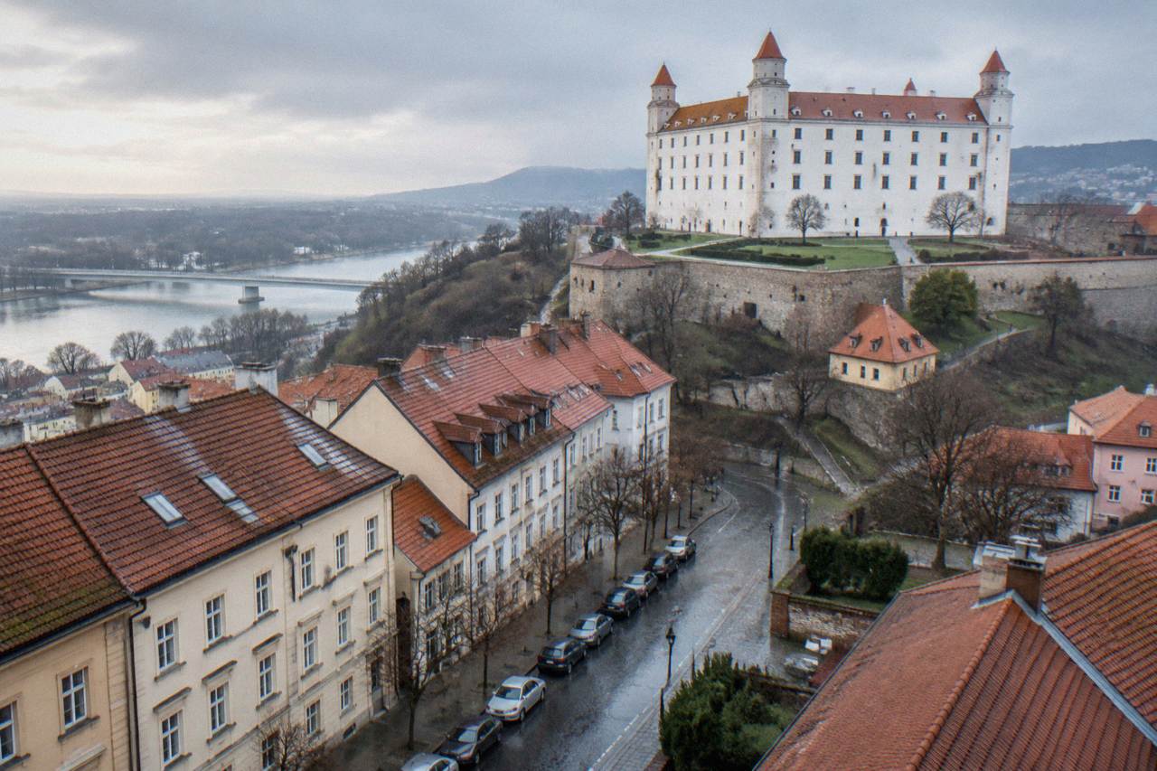 Cars parked along a quiet street below Bratislava Castle on a bright morning