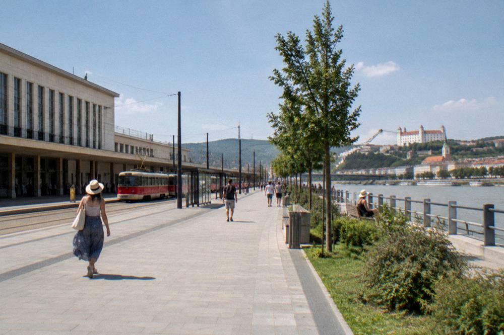 A riverside promenade under a summer sky with people strolling