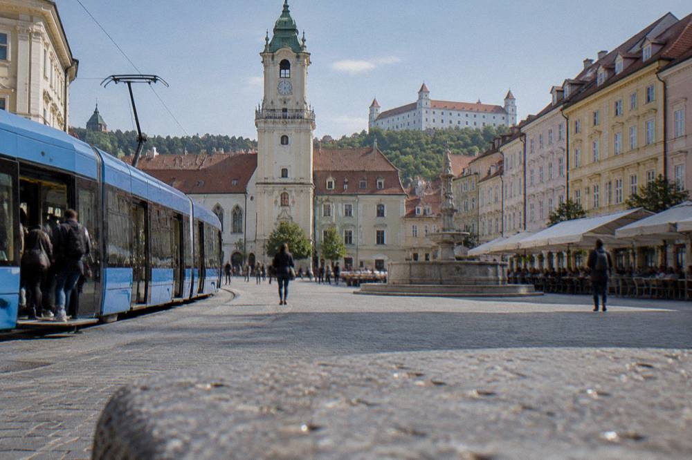 Blue tram curving through a Bratislava street with passengers boarding