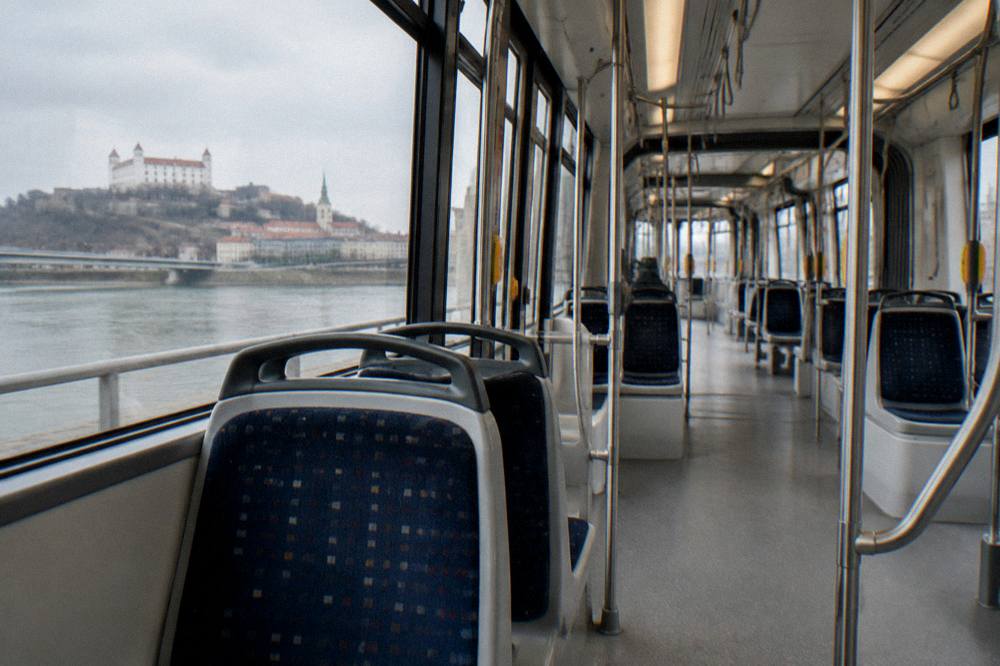 A tram interior with handrails and empty seats during a daytime ride through Bratislava