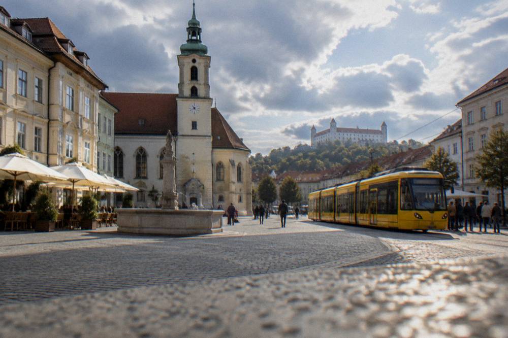 A yellow tram moving along a street in Bratislava with passengers waiting
