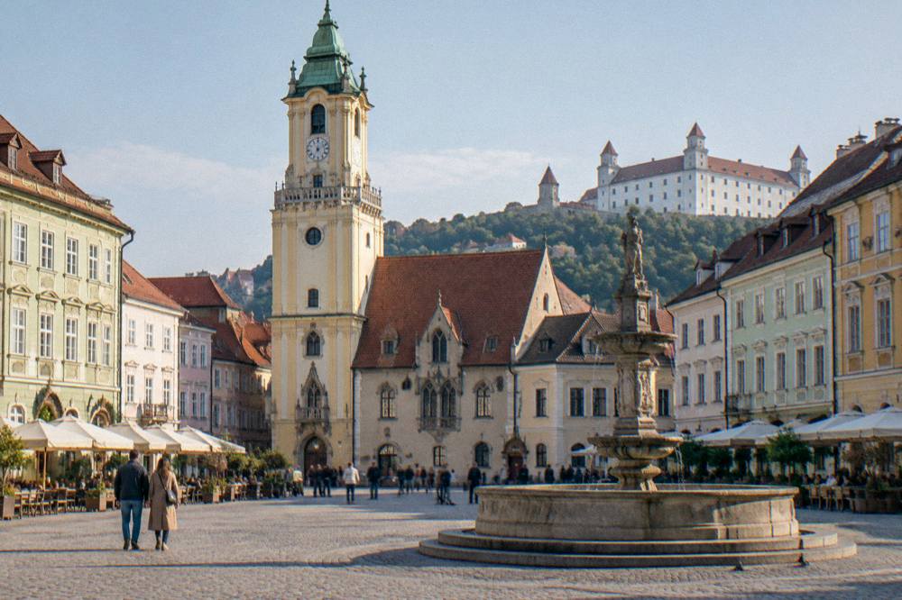 Fountain and colourful building facades on a main square in late afternoon light