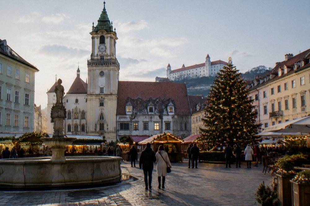 Festive market stalls and a decorated tree on a Bratislava square in the evening