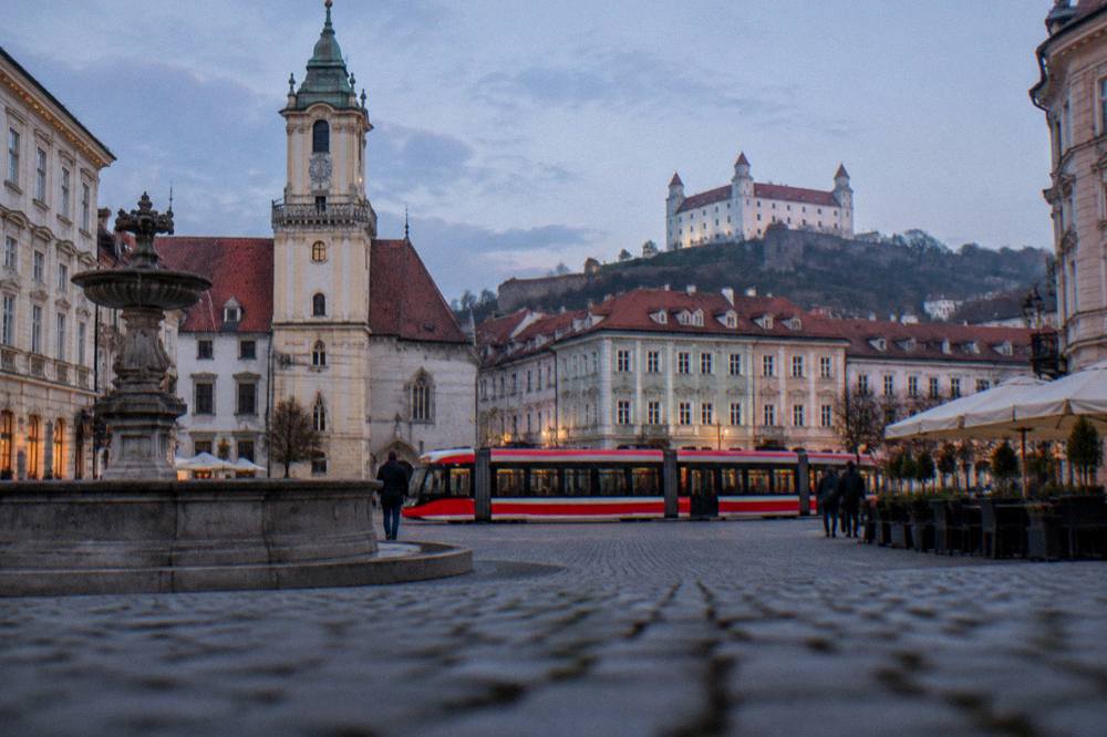A tram crossing a Bratislava street with the castle hill in the background