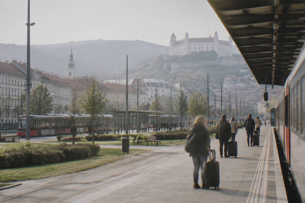 A railway platform with a departing train and passengers waiting with luggage