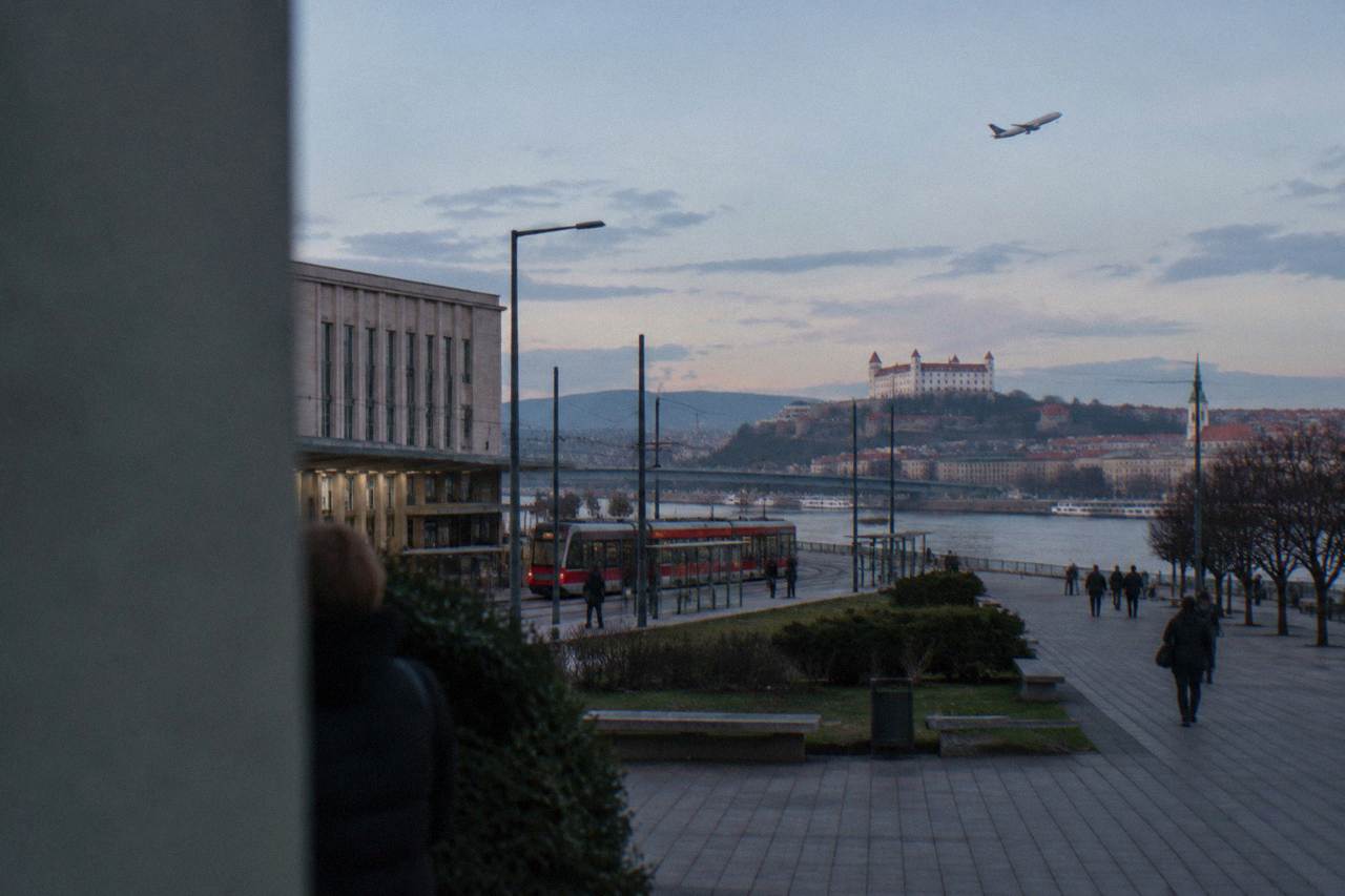 An airliner climbing over a flat landscape with a river and a distant city skyline