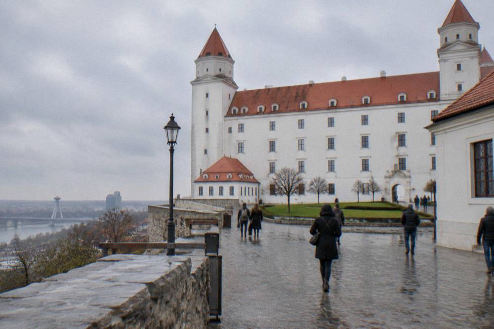 Wide courtyard walls of Bratislava Castle with walkers on the paved square