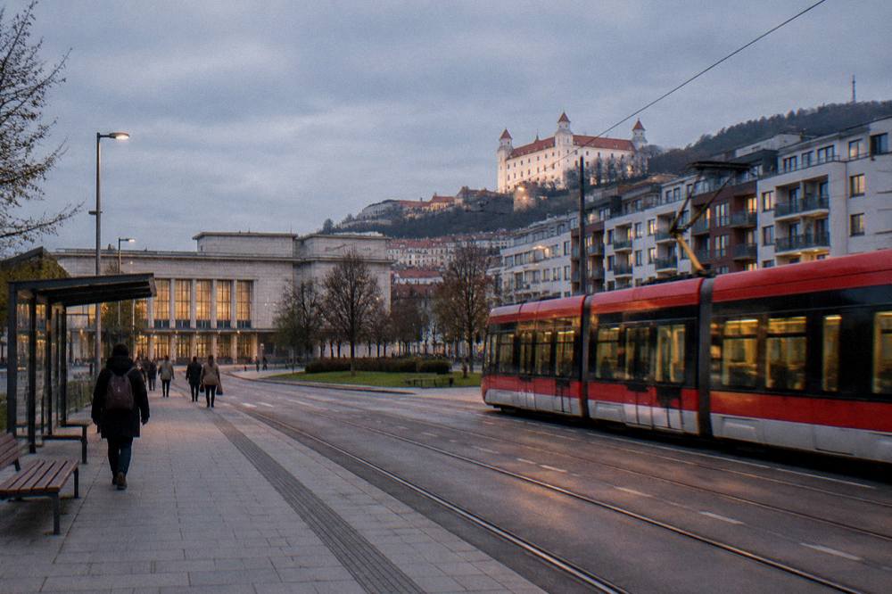 A tram passing modern apartment buildings near a railway station at dusk
