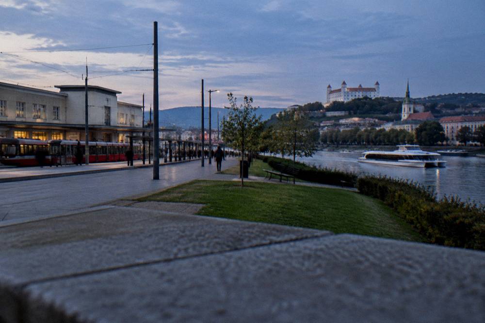 A passenger catamaran cruising along a wide river between green banks