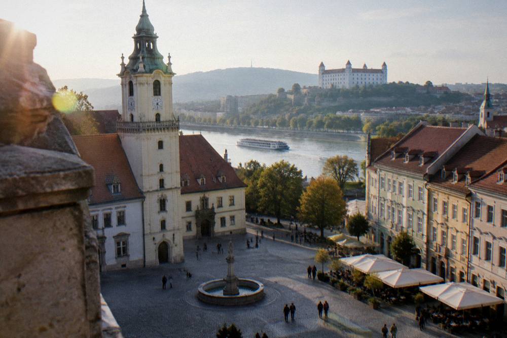 A riverboat approaching a city waterfront with a castle on a hill above