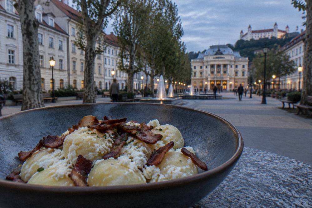 Small potato dumplings coated in white sheep cheese with crispy bacon pieces in a deep bowl