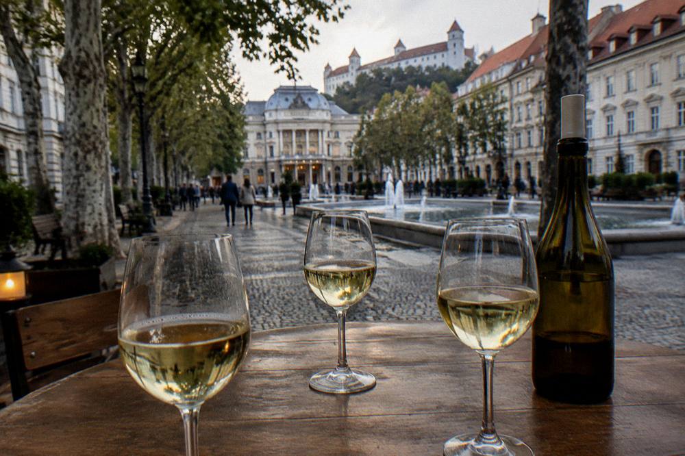 Three glasses of white wine on a wooden cellar table next to a bottle