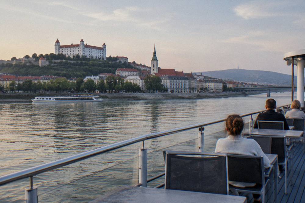 A river cruise boat with an open upper deck on the Danube at dusk in Bratislava