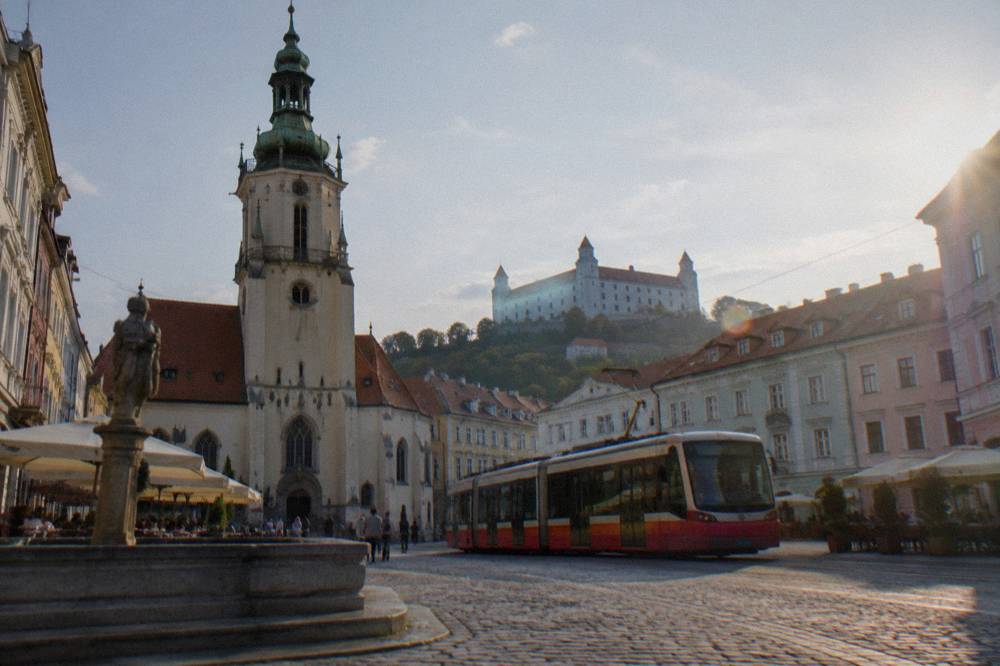 A tram passing through a Bratislava street with the castle in the background
