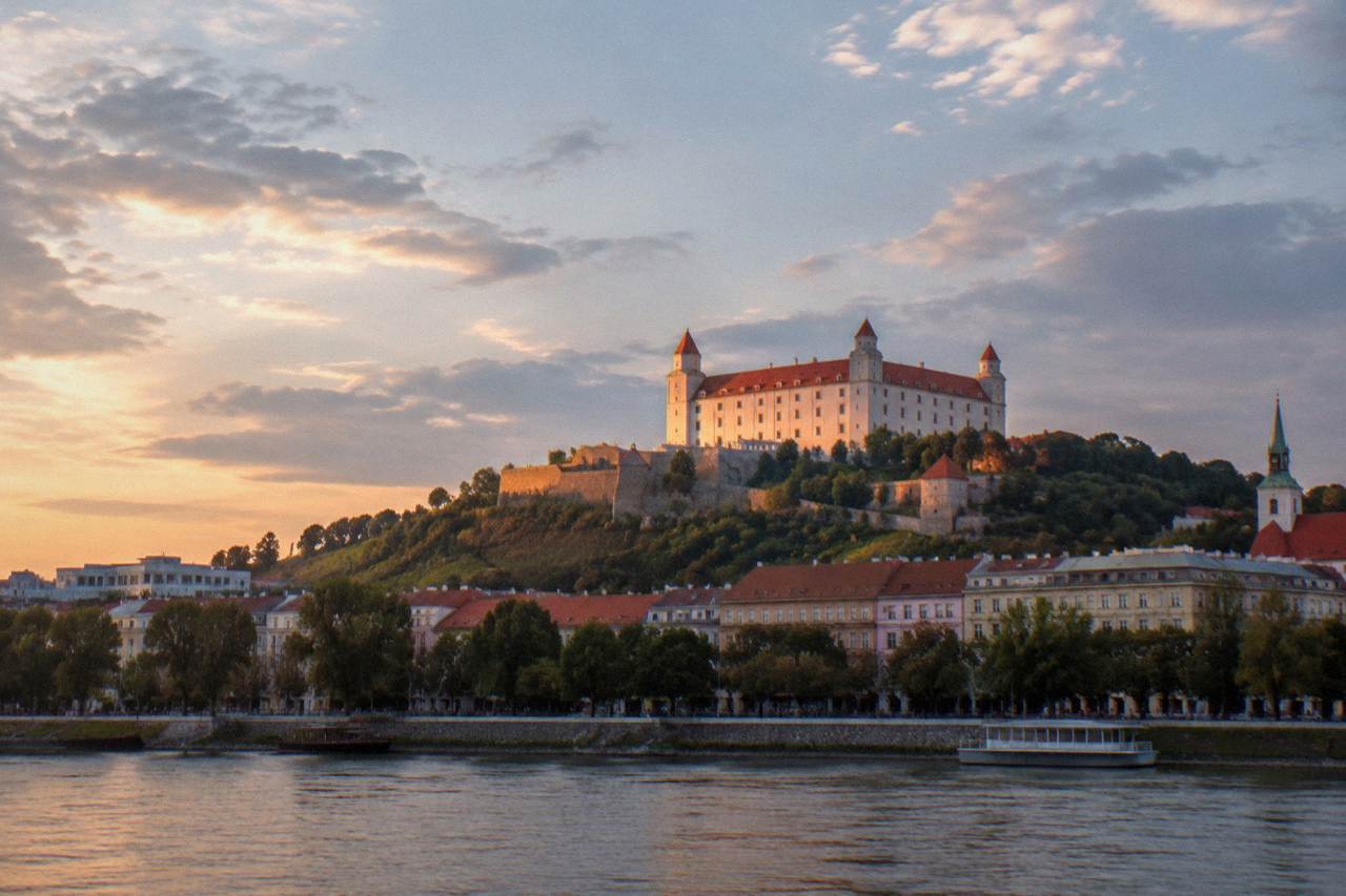 Bratislava Castle seen from below at dusk, with the hill lit against a pale evening sky