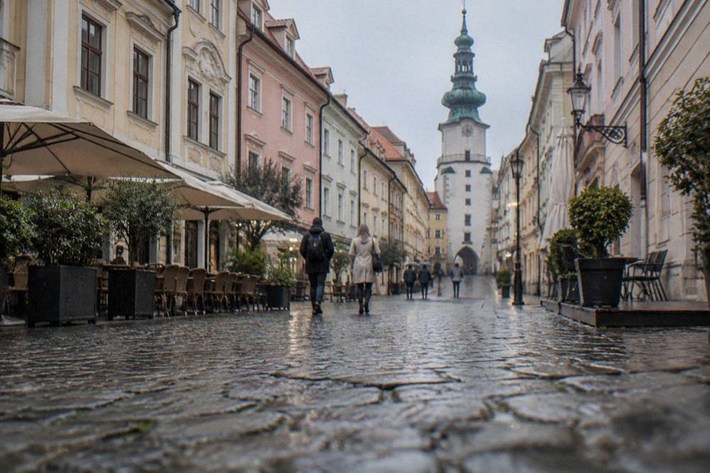 Visitors walking past colourful baroque townhouses on a narrow Old Town street in Bratislava