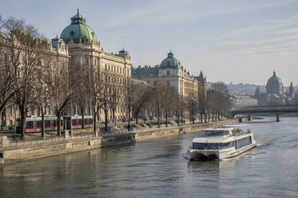 A white river catamaran cruising along the Danube between forested banks